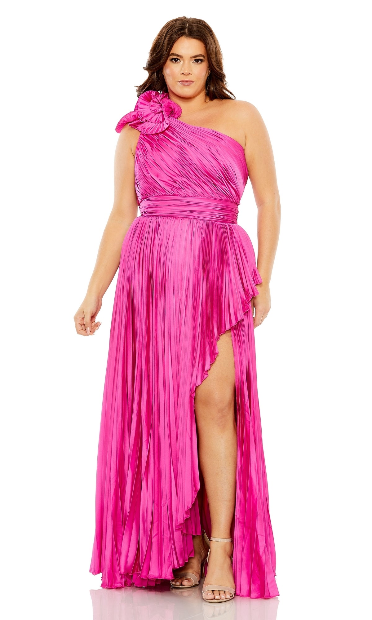 A woman wears the Long Plus-Size Formal Dress 77003 by Mac Duggal, a bright pink one-shoulder A-line gown with pleats, dramatic shoulder detail, high slit, and styled with strappy heeled sandals.